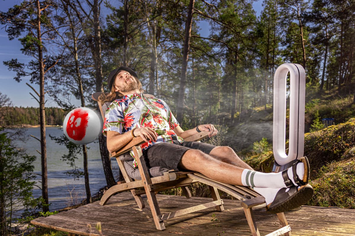 Aurinkotuolissa lepäilevä mies vierellään ilmaa puhaltava tuuletin