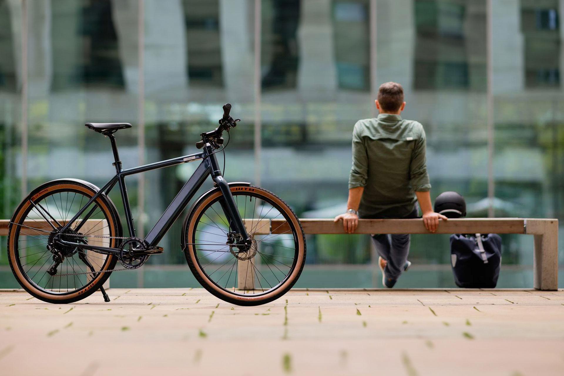 Pyöräilijä istuu penkillä vieressään kypärä ja reppu. Etualalla polkupyörä. Kuva: Coboc